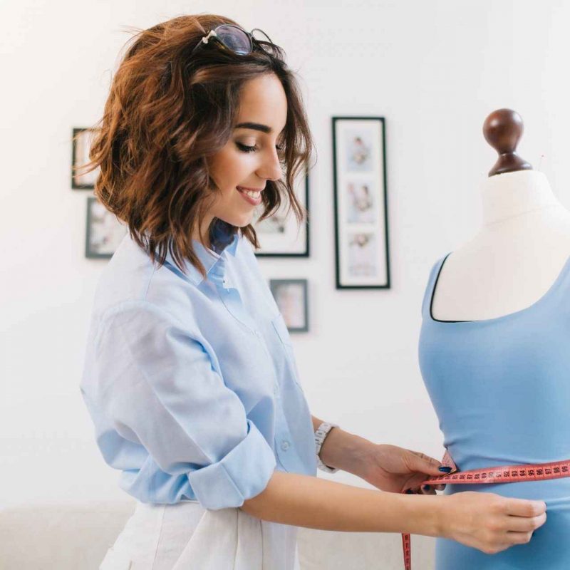 a-brunette-girl-in-a-blue-shirt-is-working-in-the-workshop-studio-she-makes-fitting-on-the-blue.jpg